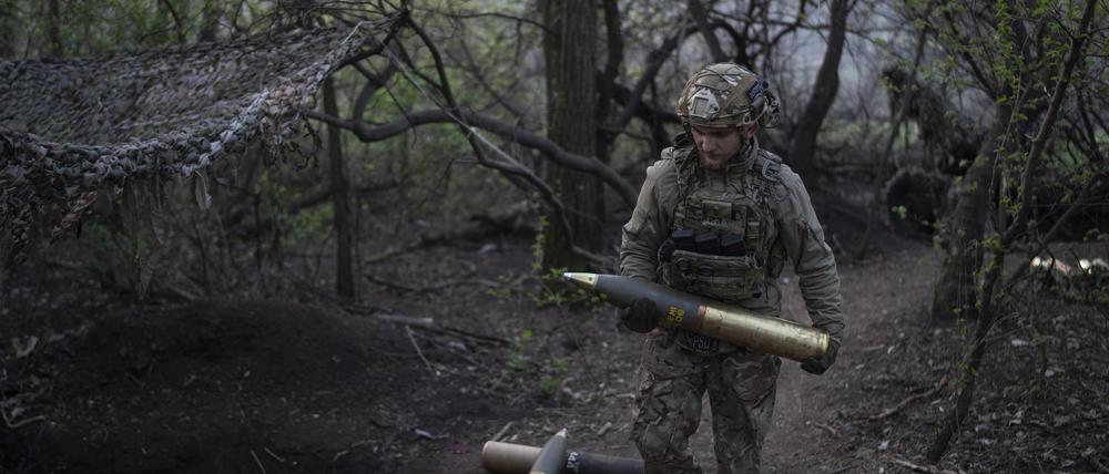 Ein ukrainischer Soldat trägt eine Granate für eine Haubitze an der Front.