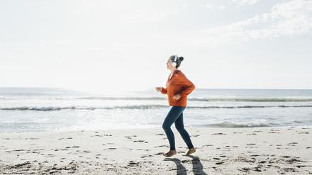 Eine junge Frau joggt barfuß am Strand entlang.