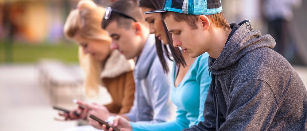 Group of teenagers sitting outdoors using their mobile phones