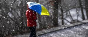 Eine Spaziergängerin geht mit einem Regenschirm während eines Schauers bei Sonnenschein im Volkspark Wilmersdorf spazieren.