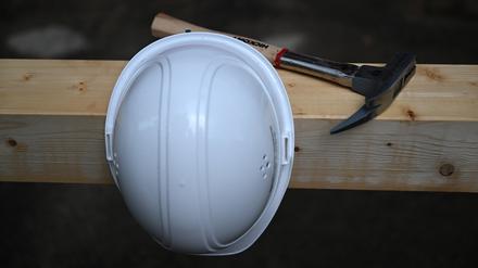 ARCHIV - 26.08.2022, Brandenburg, Potsdam: Ein Hammer liegt auf einer Baustelle auf einem Holzbalken hiner einem an einem Nagel aufgehängten Bauhelm. (zu dpa: «Arbeitssicherheit in Betrieben: Mehr Beanstandungen, weniger Bußgelder») Foto: Soeren Stache/dpa +++ dpa-Bildfunk +++