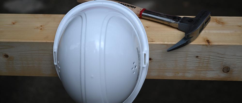 ARCHIV - 26.08.2022, Brandenburg, Potsdam: Ein Hammer liegt auf einer Baustelle auf einem Holzbalken hiner einem an einem Nagel aufgehängten Bauhelm. (zu dpa: «Arbeitssicherheit in Betrieben: Mehr Beanstandungen, weniger Bußgelder») Foto: Soeren Stache/dpa +++ dpa-Bildfunk +++