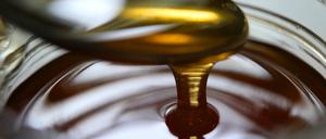 Honig fließt von einem Löffel in ein Honigglas.