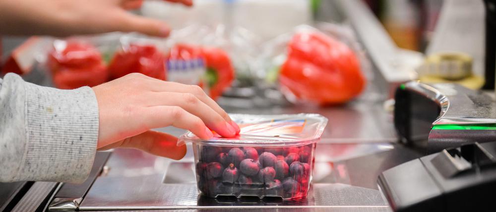 Eine Kassiererin scannt Heidelbeeren an der Kasse eines Supermarktes.  