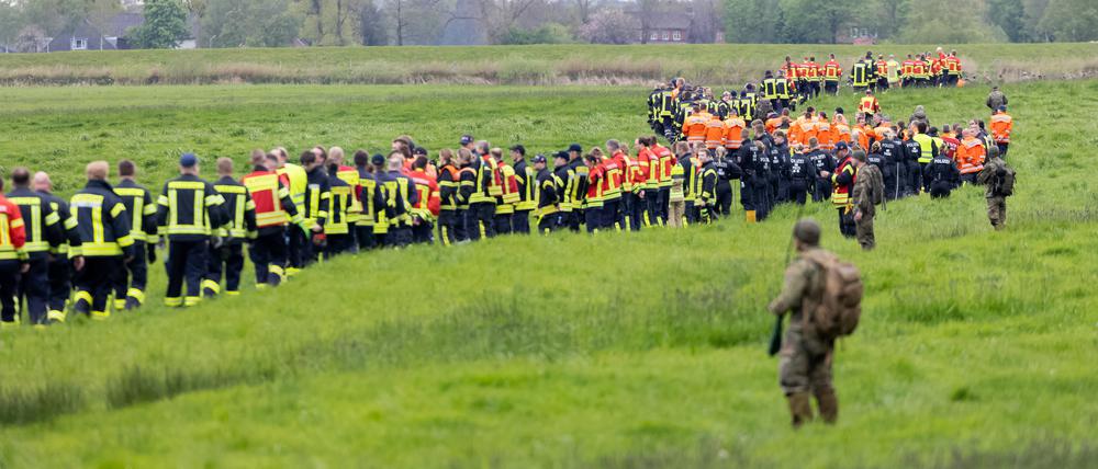 Soldaten der Bundeswehr und Einsatzkräfte von Feuerwehr und Polizei stellen sich auf, um ein Feld abzusuchen. 
