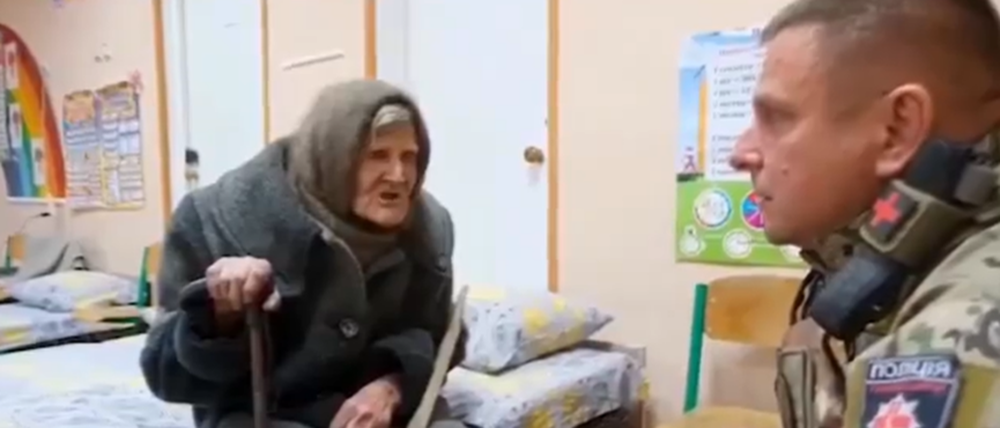 Eine 98-jährige ukrainische Frau sitzt auf einem Bett und spricht mit einem Mann in Uniform.