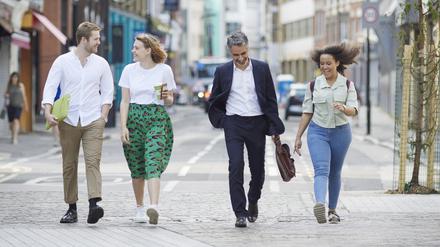 Smiling confident coworkers walking on city street with smart phones and laptop discussing project
Mid