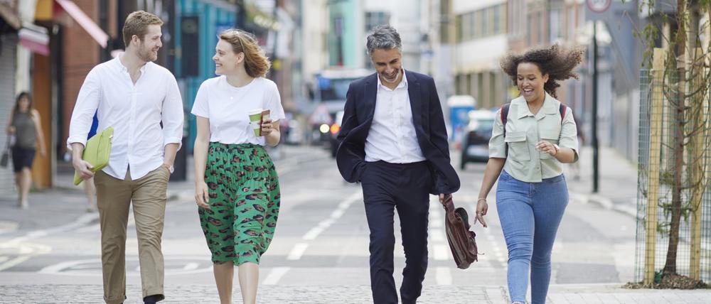Smiling confident coworkers walking on city street with smart phones and laptop discussing project
Mid