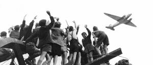 Luftbrücke live: Von einem Trümmerberg winken West-Berliner Kinder einem Propellerflugzeug zu.
