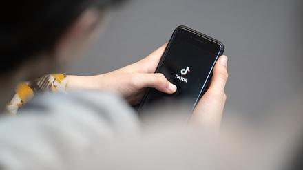 Eine Jugendliche schaut auf ein Smartphone mit angezeigtem TikTok Logo. Auf der Online-Plattform gibt es vermehrt extremistische Influencer, die Jugendliche gezielt ködern wollen.
