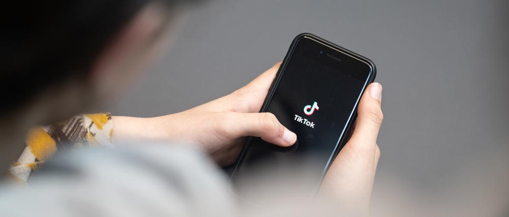 Eine Jugendliche schaut auf ein Smartphone mit angezeigtem TikTok Logo. Auf der Online-Plattform gibt es vermehrt extremistische Influencer, die Jugendliche gezielt ködern wollen.