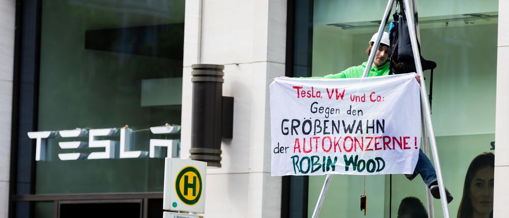 Ein Aktivist hängt bei einer Protestaktion der Umwelt- und Naturschutzorganisation Robin Wood gegen die geplante Tesla-Werkserweiterung in Grünheide vor dem Tesla Store in der Mall of Berlin in einem Tripod und hält ein Transparent.
