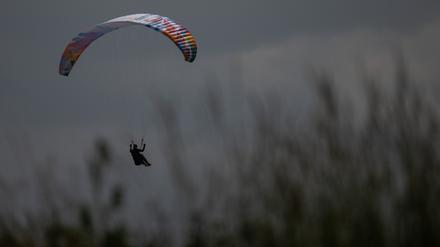 ARCHIV - 21.06.2023, Hessen, Gersfeld: Ein Gleitschirmflieger wird von der Sonne angeschienen während er in einer Wiese landet. 