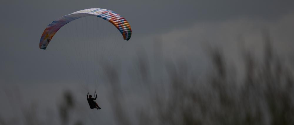 ARCHIV - 21.06.2023, Hessen, Gersfeld: Ein Gleitschirmflieger wird von der Sonne angeschienen während er in einer Wiese landet. 