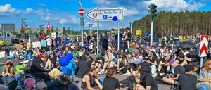11.05.2024, Brandenburg, Grünheide: Viele Teilnehmer einer Protestveranstaltung sitzen auf einer sitzen und stehen auf einer Straße vor dem Werk von Tesla. Nach teils heftigen Auseinandersetzungen am 10.05.2024 am Tesla-Werksgelände in Grünheide bei Berlin stellt laufen derzeit neue Proteste gegen das US-Unternehmen. Foto: Patrick Pleul/dpa +++ dpa-Bildfunk +++