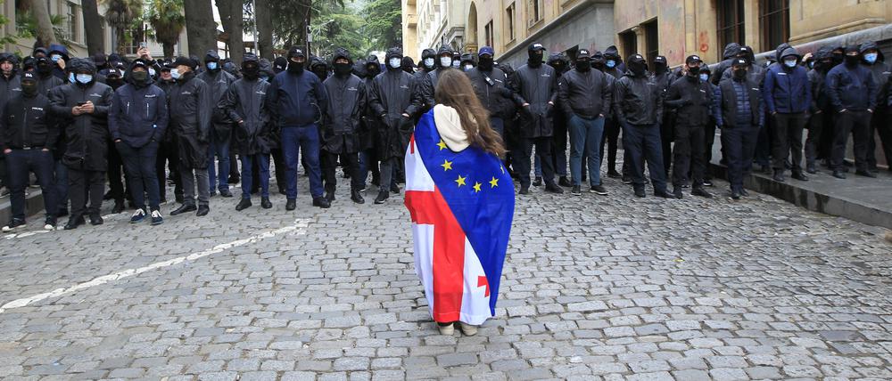 14.05.2024, Georgien, Tiflis: Ein Demonstrant mit drapierten georgischen National- und EU-Flaggen steht vor der Polizei, die den Weg zum Parlamentsgebäude blockiert, während eines Protestes der Opposition gegen das «russische Gesetz». Begleitet von Protesten hat das georgische Parlament die Verabschiedung eines umstrittenen Gesetzes begonnen, das ausländischen Einfluss auf die Zivilgesellschaft beschneiden soll. Foto: Shakh Aivazov/AP/dpa +++ dpa-Bildfunk +++