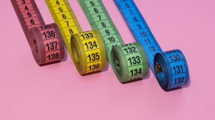 Vier bunte Maßbänder vor einem pinken Hintergrund. Wer mit Ozempic, Wegovy und Co. behandelt wird, nimmt ab. Nur, für wie lange?
