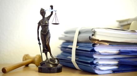 Eine modellhafte Nachbildung der Justitia steht neben einem Holzhammer und einem Aktenstapel.