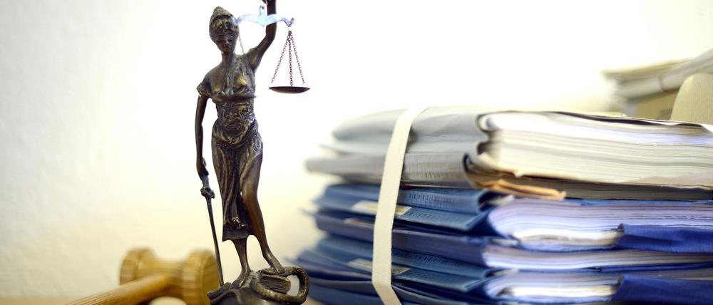 Eine modellhafte Nachbildung der Justitia steht neben einem Holzhammer und einem Aktenstapel.