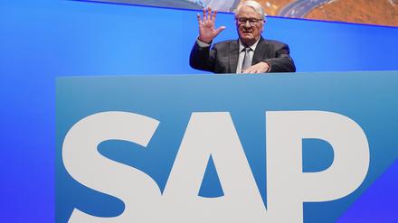 Hasso Plattner steht winkend hinter einer Tafel mit einem großen SAP-Schriftzug.
