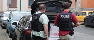 Nach einer Wohnungsdurchsuchung verladen Polizisten einen Karton mit sichergestellten Gegenständen in einen Wagen.