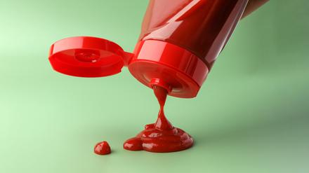 Eine Ketchupflasche wird vor grünem Hintergrund ausgeschüttet.