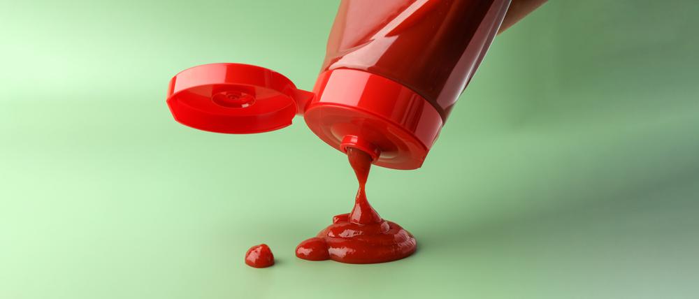 Eine Ketchupflasche wird vor grünem Hintergrund ausgeschüttet.