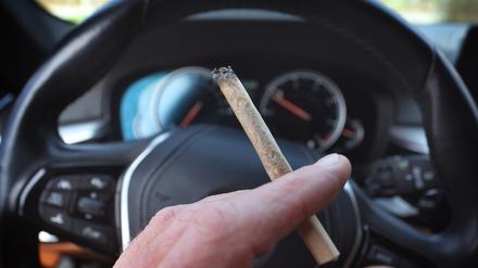 Eine Hand hält vor dem Steuer eines Autos einen Joint (Archivbild vom 20.03.2024).