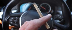 Ein Mann sitzt mit einem Joint zwischen den Fingern am Steuer eines Autos.