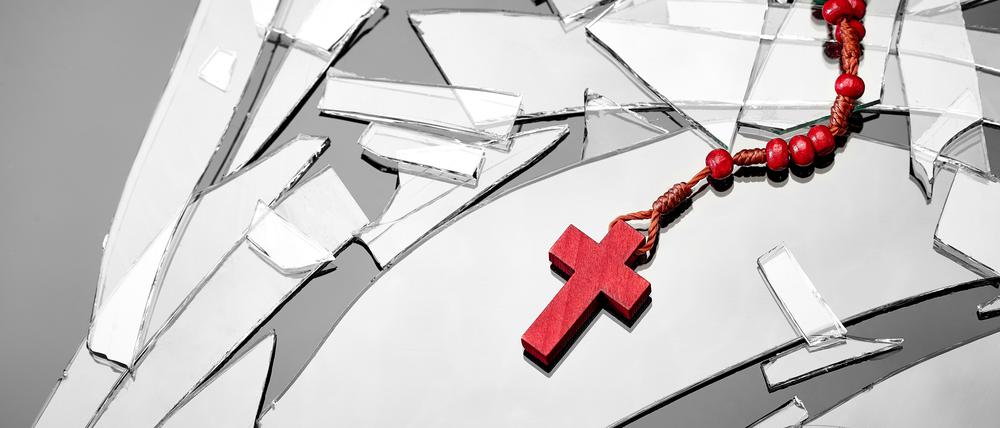 Rotes Kruzifix auf Glassplittern. Die christlichen Kirchen verlieren immer mehr Mitglieder.