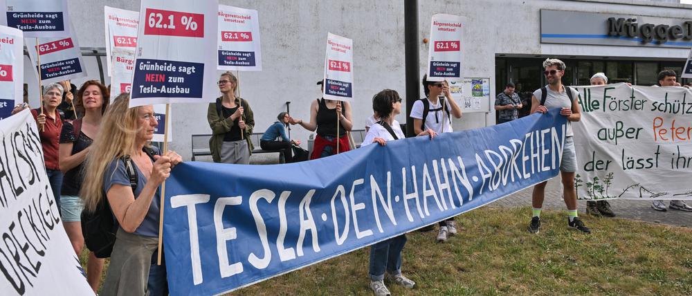 16.05.2024, Brandenburg, Grünheide: Teilnehmer der Bündnisinitiative «Tesla den Hahn abdrehen» protestieren vor der Müggelspreehalle in Hangelsberg, einem Ortsteil von Grünheide, wo am späten Nachmittag die Gemeindevertreter über die Erweiterungspläne der Tesla-Fabrik in Grünheide abstimmen wollen. Foto: Patrick Pleul/dpa +++ dpa-Bildfunk +++