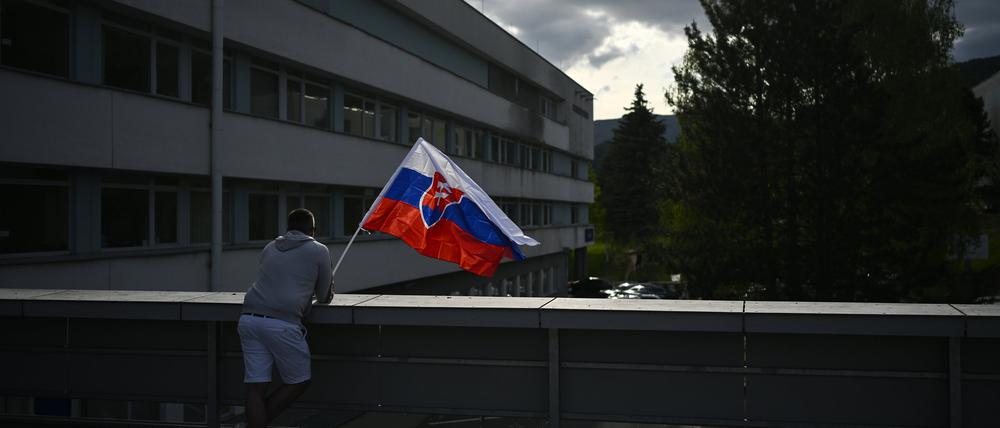 Slowakei, Banska Bystrica: Ein Mann schwenkt die slowakische Nationalflagge vor dem F. D. Roosevelt Universitätskrankenhaus, in dem der angeschossene und verwundete slowakische Premierminister Fico behandelt wird.