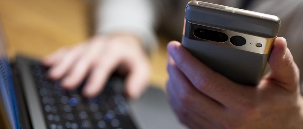 Ein Mann sitzt am Laptop und hält ein Smartphone mit in der Hand.