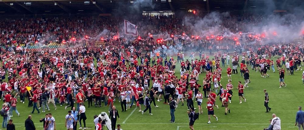 Zahlreiche Fans feiern ausgelassen den Aufstieg ihrer Mannschaft auf dem Spielfeld.