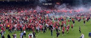 Zahlreiche  Fans feiern ausgelassen den Aufstieg ihrer Mannschaft auf dem Spielfeld.