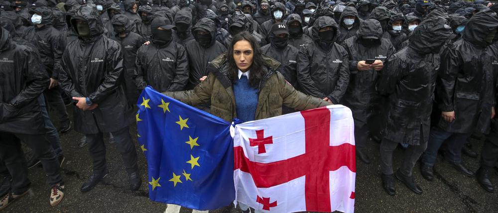 Eine Frau mit einer georgischen Nationalfahne und einer EU-Fahne steht vor Polizisten (Symbolbild).