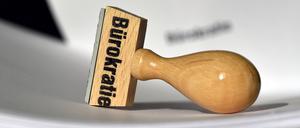 Ein Stempel mit der Aufschrift „Bürokratie“ liegt auf Papieren.