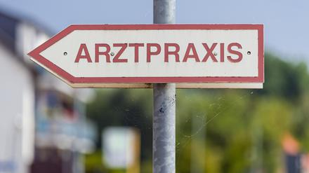 Ein Schild mit der Aufschrift „Arztpraxis“ steht an der Straße.