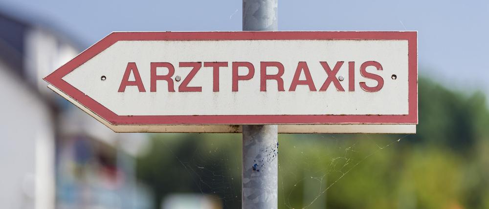 Ein Schild mit der Aufschrift „Arztpraxis“ steht an der Straße.