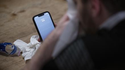 Ein Mann hält ein Taschentuch in einer Hand und ein Telefon mit dem Schriftzug „Arzt“ in der Anderen.