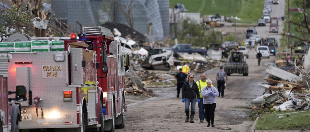 Menschen gehen in Greenfield, Iowa, eine Straße entlang, vorbei an Schäden nach einem Tornado.