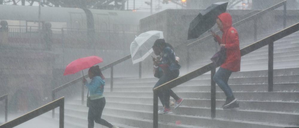Vor dem Kölner Hauptbahnhof kämpfen Menschen mit starken Regenfällen.