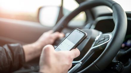 Eine Person sitzt am Steuer eines Autos und tippt dabei auf ihrem Smartphone.