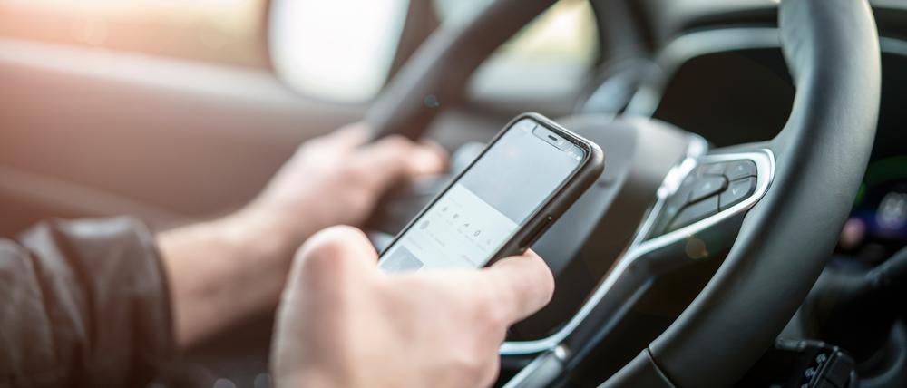 Eine Person sitzt am Steuer eines Autos und tippt dabei auf ihrem Smartphone.