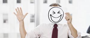 Ein Geschäftsmann hält ein Papier mit einem gemalten, breit grinsenden Smiley vor seinem Gesicht.