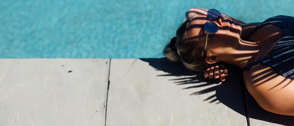 Eine Frau liegt am Rand eines Pools im Schatten.