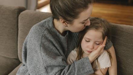 Ein Mutter hält ihre Tochter auf einem Sofa im Arm.