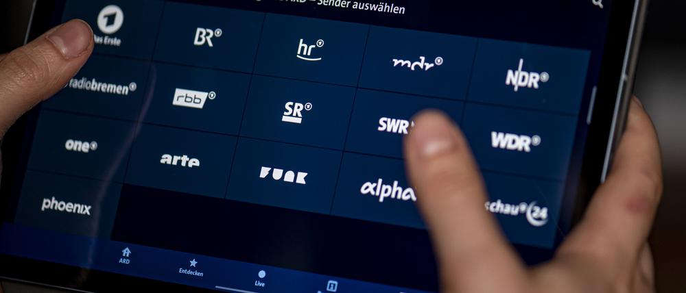 Ein Mann benutzt die ARD-Mediathek App auf einem Tablet, auf dem unter anderem die Sender BR, hr, mdr, NDR, phoenix, rbb, SR, SWR, WDR und arte zu sehen sind. 