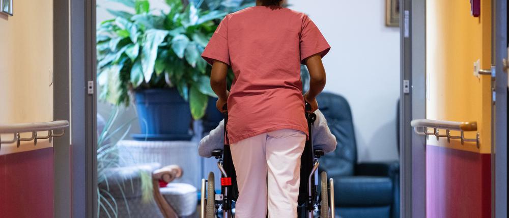 Eine Bewohnerin eines Pflegeheims wird von einer Pflegerin einen Gang entlang geschoben.