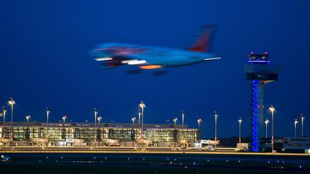Ein Passagierflugzeug landet neben dem hell erleuchteten Berlin Brandenburg Airport Willy Brandt (BER).